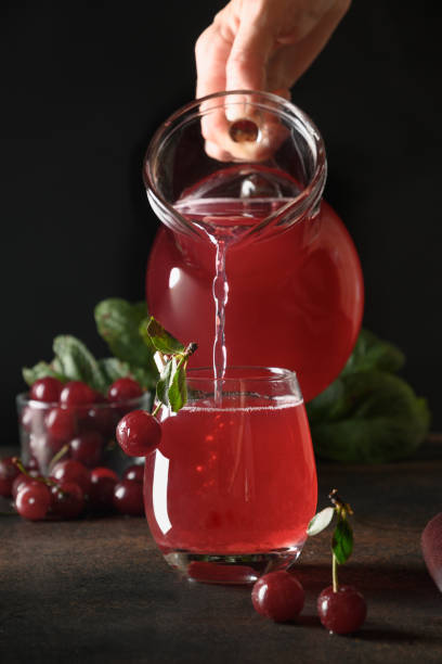 Pouring red cherry compote in glass on black background. Vertical format.