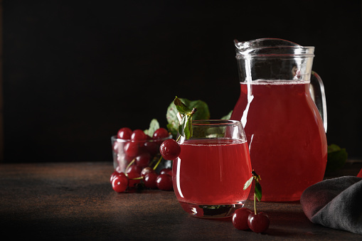 Red cherry summer compote in glass on dark background. Close up. Freshness summer homemade beverage.