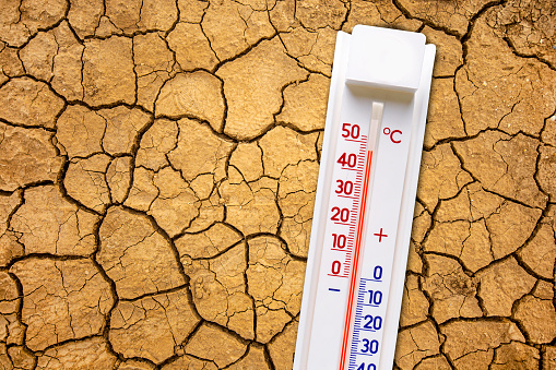 Global warming concept with a thermometer and dry cracked earth texture.