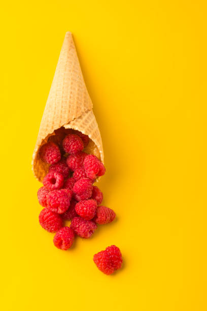 istock Minimalism. Raspberry explosion in a waffle cone on a yellow table. View from above. Healthy food concept. Vertical position. 1333257743