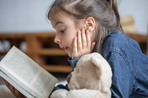 istock Little girl reads a book with a teddy bear. 1333258088
