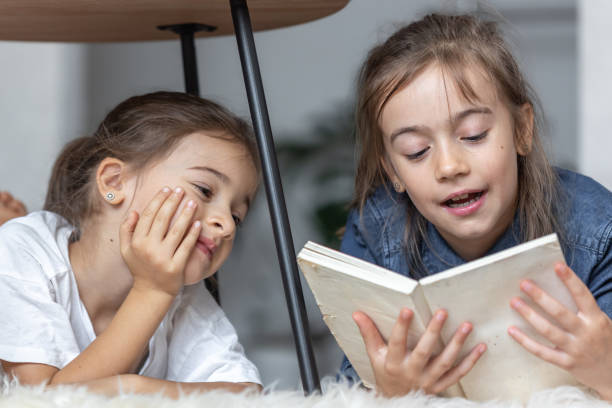 istock Two little sisters are reading a book lying on the floor on a cozy blanket. 1333258182