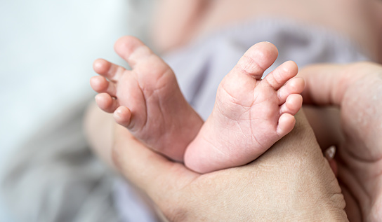 A close up view of unrecognizable Caucasian parents holding her cute baby girl's feet.