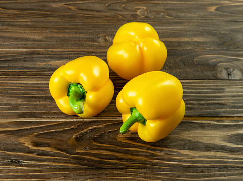 Three whole fresh yellow bell peppers close-up on a brown wooden background.