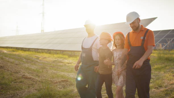 dos padres llevaron a sus hijos al trabajo. dos empleados de una planta de energía solar cuentan a los niños sobre la producción de electricidad. parque solar. concepto de energía alternativa. construcción ecológica - solar energy solar power station student alternative energy fotografías e imágenes de stock