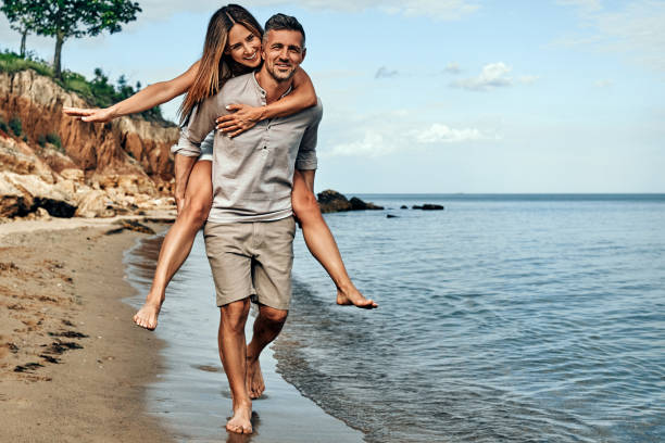 mężczyzna trzyma na rękach piękną kobietę. para spędza czas nad brzegiem morza. lato, morze, dobry nastrój. - beach couple satisfaction playing zdjęcia i obrazy z banku zdjęć