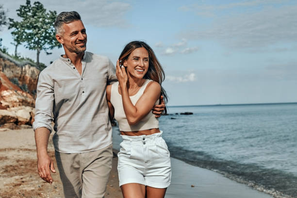 feliz pareja atractiva caminando en la hermosa playa soleada. - bien parecido fotografías e imágenes de stock