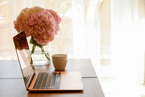 Home office concept. Designated work from home area. Feminine workspace with modern laptop and vase with flowers on table. Close up, copy space, background.