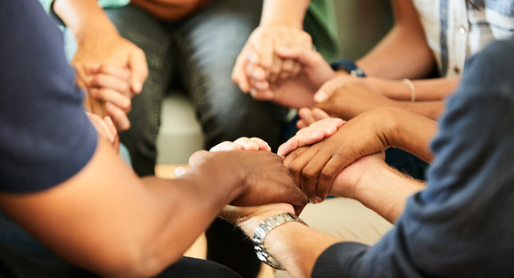 Close-up of a group of diverse people sitting in a circle and holding hands together during a support group meeting