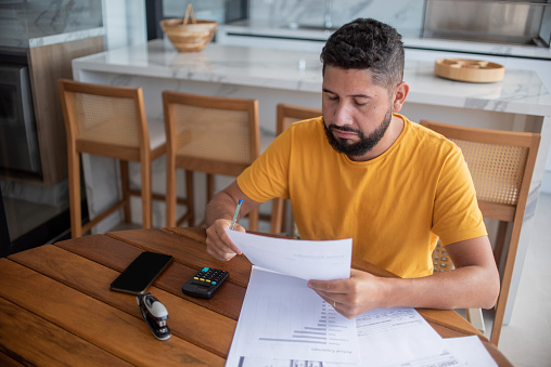 Man calculating debts at home on the porch, wearing a yellow t-shirt.