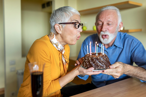 An Older Woman is Blowing the Candles on Chocolate Cake and Making a Wish for her Birthday.