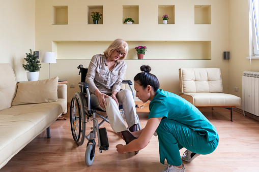 La anciana enferma en silla de ruedas está recibiendo ayuda de una enfermera joven en visita domiciliaria. photo