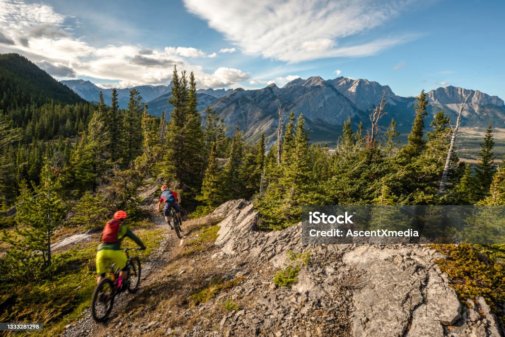 View of mountain bikers following trail down mountain Sunny Canadian Rockies in the distance The Way Forward Stock Photo