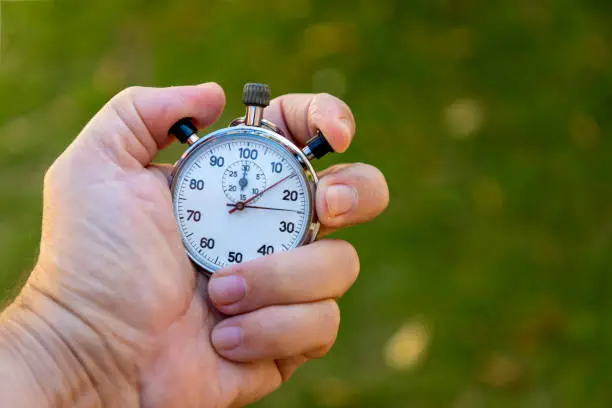 Photo of hand holding antique stopwatch with blurred green background.