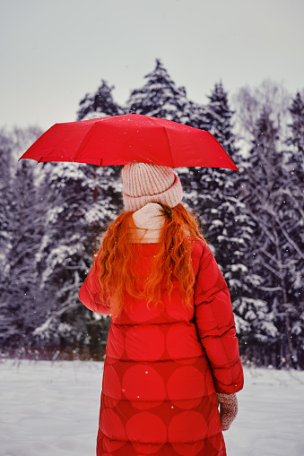 A happy woman stands with a red umbrella in her hands, a winter park with snow-covered trees