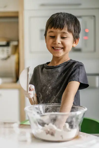 Photo of The child cooks in the kitchen. Sifts the flour.
