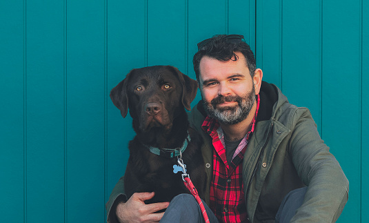 Portrait of man and dog in front of teal wall