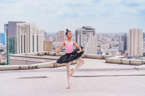 asian girl ballerina dancer performing ballet dance on rooftop of highrise building in city