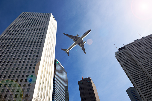 Low angle view of skyscrapers with airplane flying over modern buildings against blue sky.