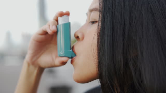 Asian woman using asthma inhaler