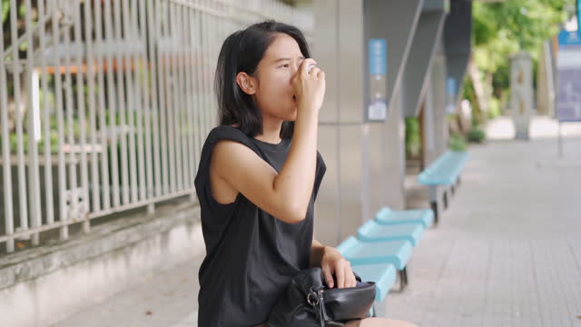 Asian woman using asthma inhaler at bus stop