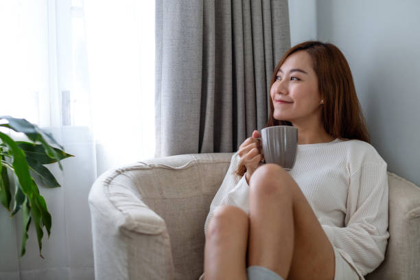 istock a beautiful asian woman looking outside the window while drinking hot coffee and relaxing on a sofa in bedroom at home 1333316132