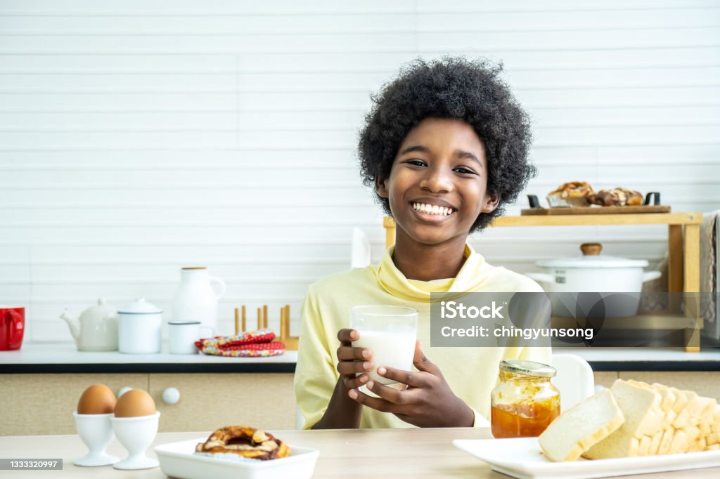 Child having breakfast. Happy cute African-American boy drinking milk and eating bread with egg. Kids eat on sunny morning. Healthy balanced nutrition for young kids. Child Stock Photo