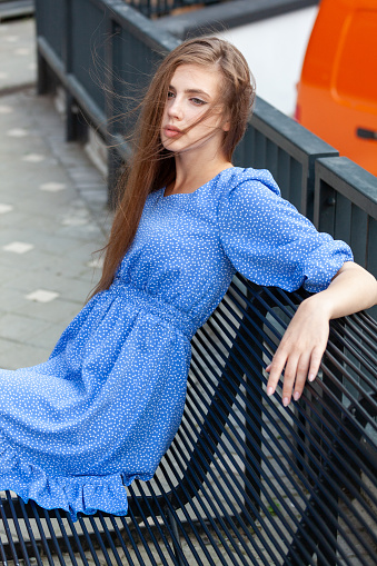 Outdoors portrait of an attractive 19 year old woman with long brown hair in a summer blue dress