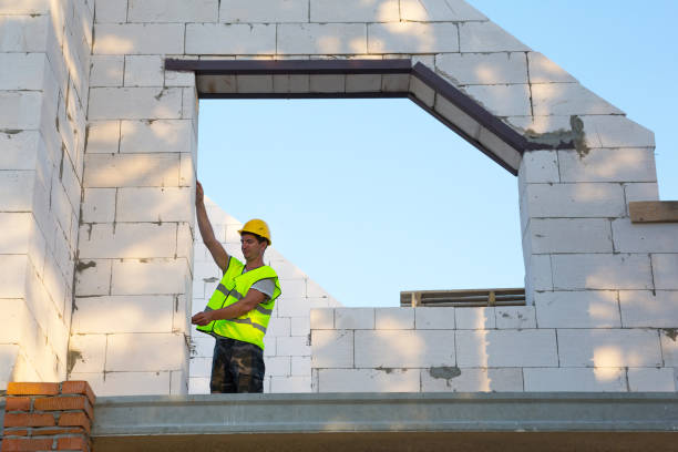 istock Construction worker at construction site measures the length of the window opening and the wall with tape measure. Cottage are made of porous concrete blocks, protective clothing - hardhat and a vest 1333323209