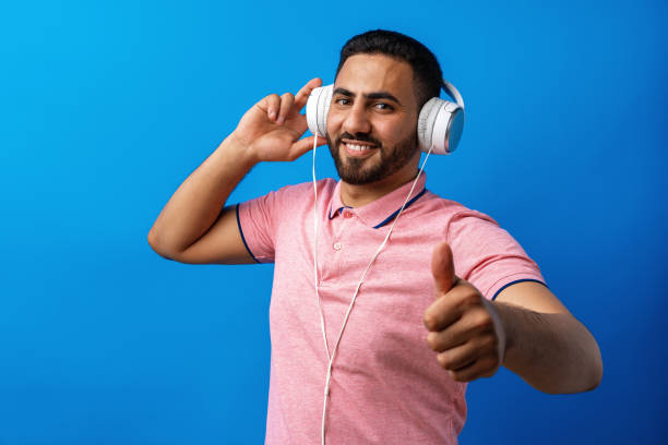 jovem homem árabe feliz com fones de ouvido ouvindo música contra fundo azul - arab style audio - fotografias e filmes do acervo