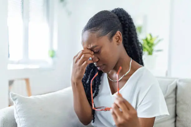 Photo of African girl in glasses rubs her eyes, suffering from tired eyes, ocular diseases concept