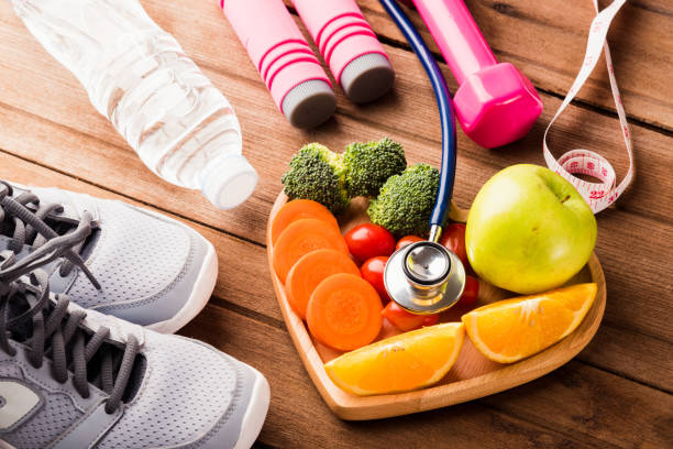 fresh organic fruits and vegetables in heart plate wood and sports equipment and doctor stethoscope stock photo