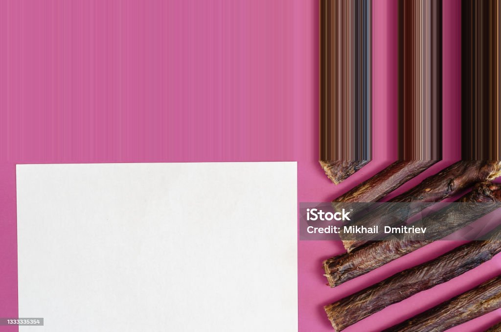 Natural chewy goodies for pets.  Dried beef esophagus. Sticks of dog treats and a blank white sheet on a pink background. Dried beef esophagus. Natural chewy goodies for pets. Stretch pixel effect Advertisement Stock Photo