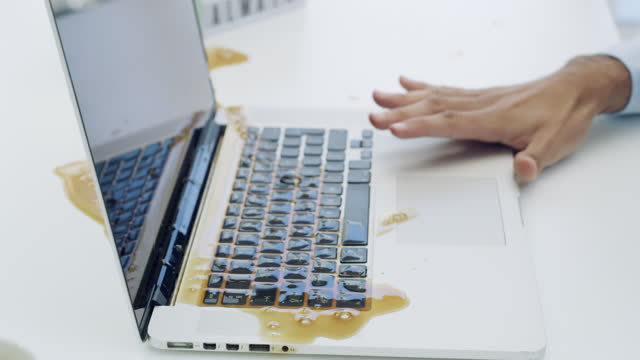 4k video footage of an unrecognizable businessman sitting in the office and spilling a cup of coffee on his laptop