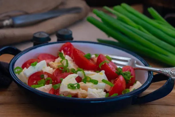 Delicious italian tomato salad made with organic cherry tomatoes and buffalo mozzarella, olive oil and chives. Served in a rustic bowl on wooden table background.