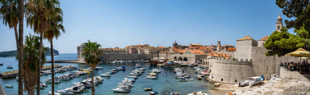 elevated and wide panoramic view over old town Dubrovnik with the marina in the foreground under blue summer sky