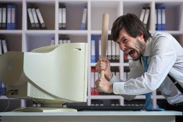 istock Angry man is destroying old computer with baseball bat in office. 1333345306
