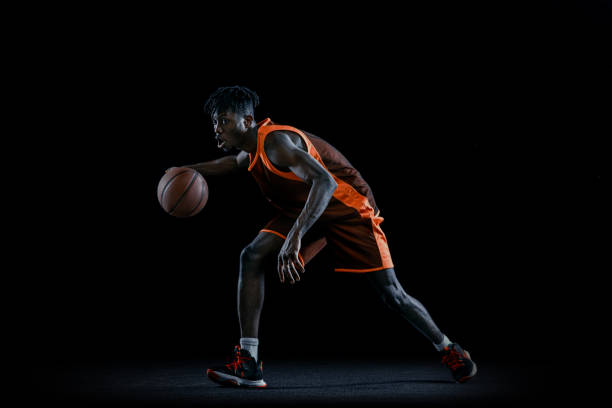 istock Studio image of young african man, basketball player practicing with ball isolated over dark studio background. 1333346382