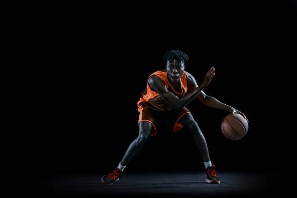 istock Front view. Young african man, basketball player practicing with ball isolated over dark studio background. 1333346385