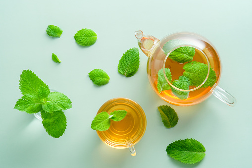 Mint tea. Flat lay teapot and teacup with green mint leaves on green background. Top view herbal beverage.
