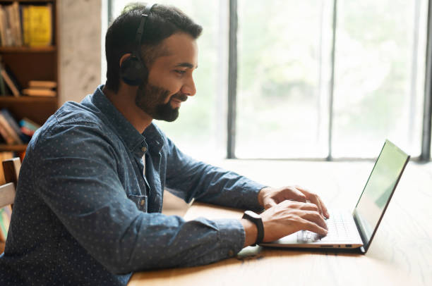 istock Young confident male Indian remote consultant wearing headset using laptop computer 1333350290
