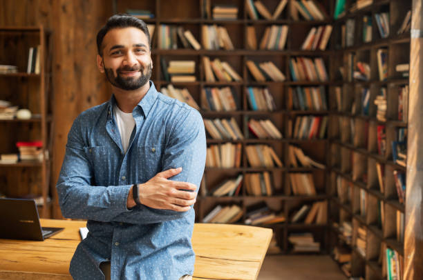 smiling bearded indian businessman stands near desk and looks at the camera - 中東人 個照片及圖片檔