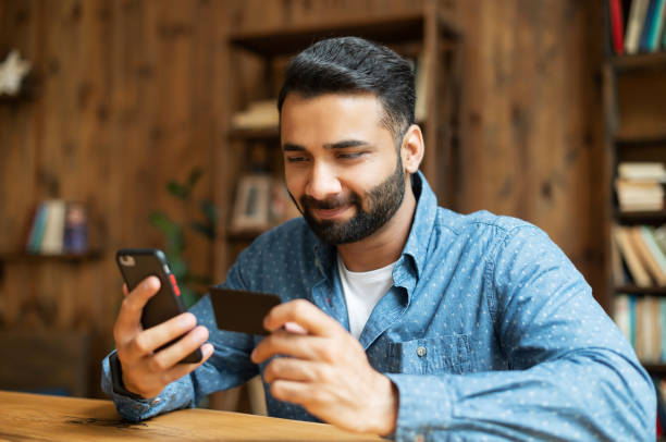 istock Young handsome Indian freelancer man using smartphone for online payment 1333350388