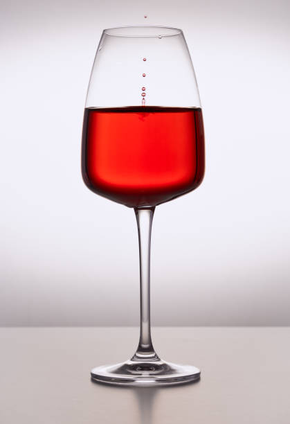 gros plan de verre de cristal de vin rouge sur fond clair avec des gouttelettes congelées. surface ondulée avec des éclaboussures. verrerie de restaurant, boisson, table, passion, amour, fête, éclaboussures d’eau. - wineglass glass crystal studio shot photos et images de collection