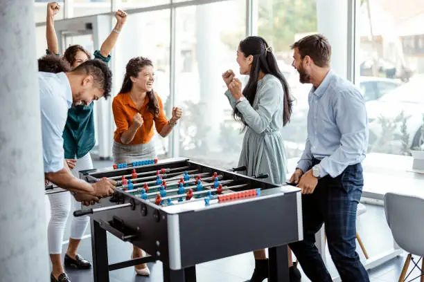 Office People Enjoying Table Soccer Game During their Free Time at the Workplace.