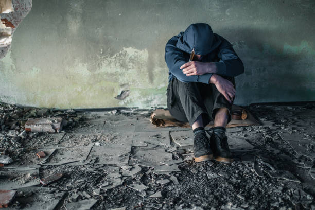 Drug addict in crisis sitting in abandoned house Young man drug addict preparing heroin drug for use with syringe and spoon drug overdose stock pictures, royalty-free photos & images