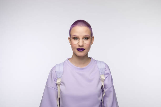 Friendly female student with short purple hair Headshot of young woman wearing lilac blouse and backpack, smiling at camera. Studio portrait on white background. purple hair stock pictures, royalty-free photos & images