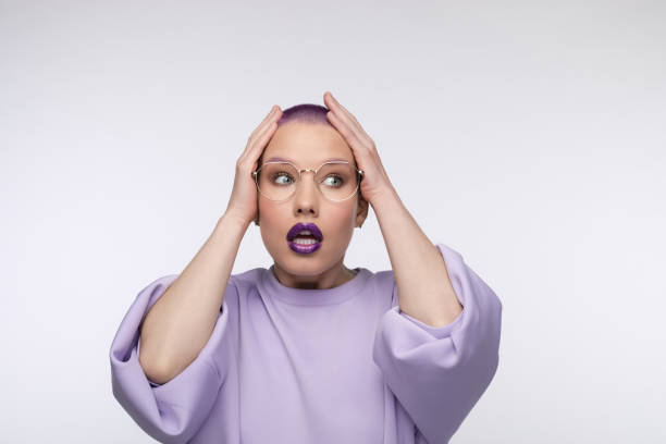 Shocked young woman with short purple hair Headshot of surprised young woman wearing lilac blouse, holding hands on head and looking away with mouth open. Studio portrait on white background. purple hair stock pictures, royalty-free photos & images
