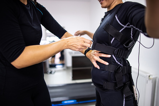Fitness trainer adjusting electro muscle stimulation suit to woman before training in exercise room
