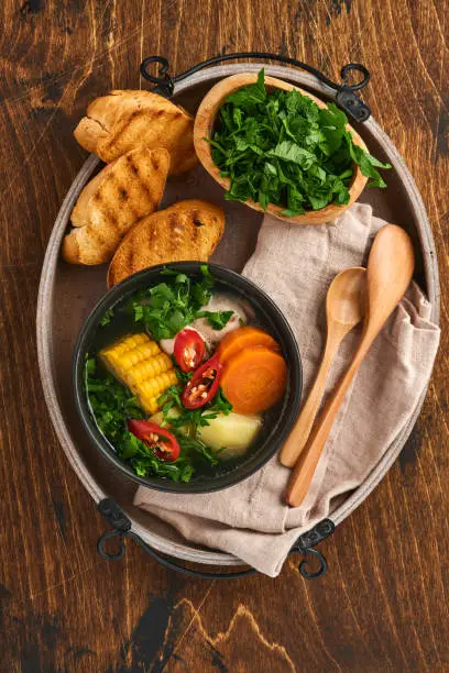 Photo of Chilean meat soup with pampkin, corn, fresh coriander and potatoes on old wooden table background. Cazuela. Latinamerican food.